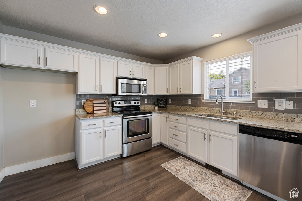 Kitchen with backsplash, appliances with stainless steel finishes, a sink, white cabinets, and dark wood-type flooring