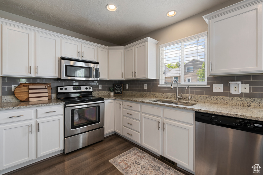 Kitchen featuring white cabinets, appliances with stainless steel finishes, a sink, tasteful backsplash, and dark wood-style floors
