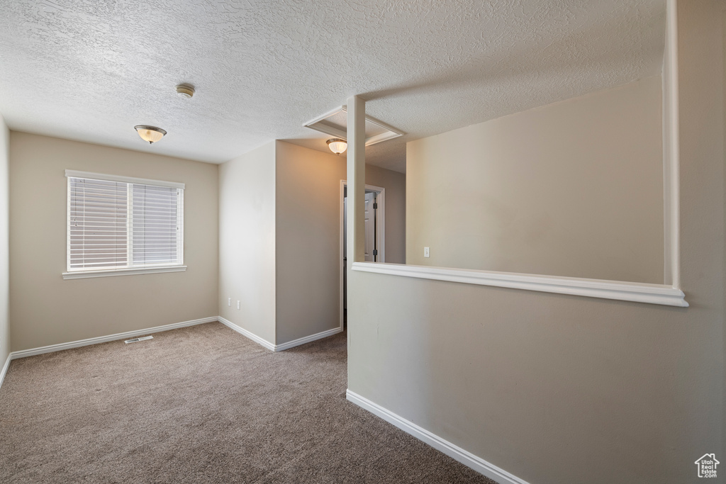 Spare room with carpet floors, baseboards, attic access, and a textured ceiling