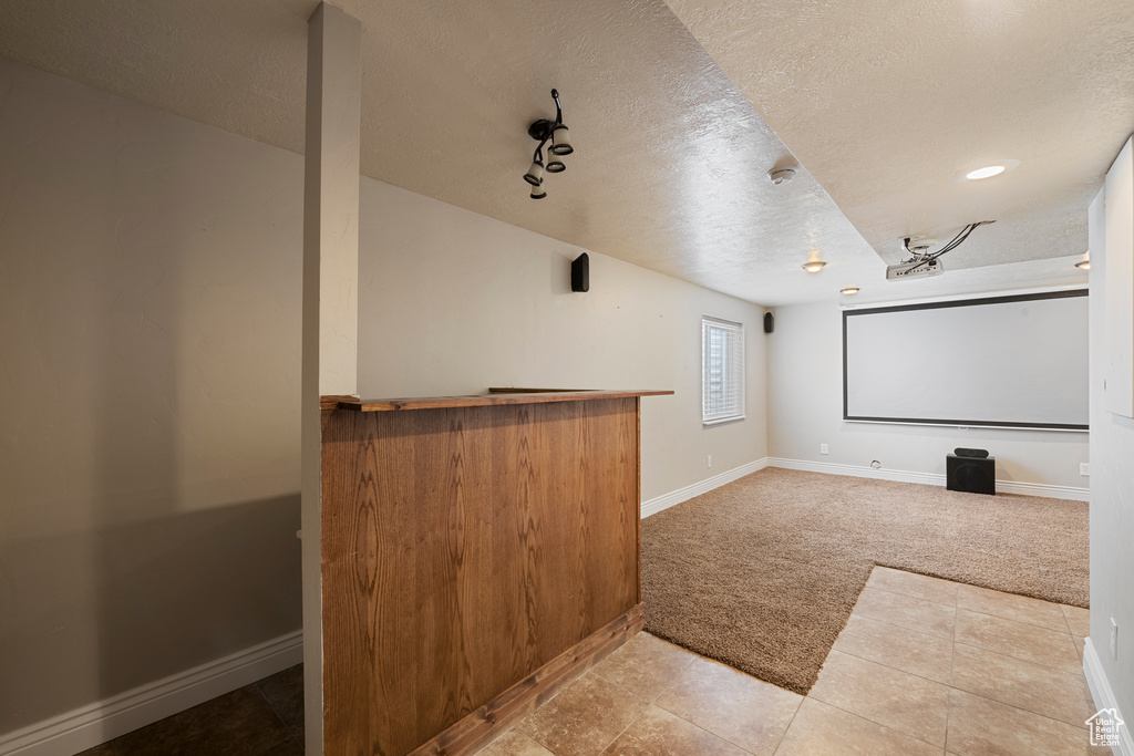 Home theater room with light carpet, a textured ceiling, baseboards, light tile patterned floors, and a bar