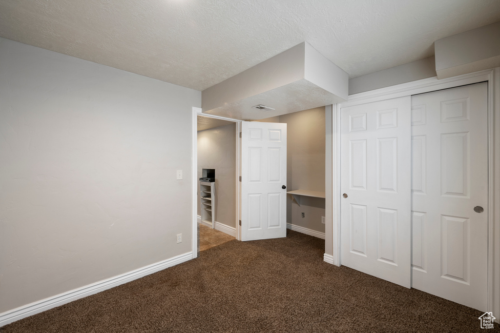 Unfurnished bedroom featuring dark carpet, baseboards, and a closet