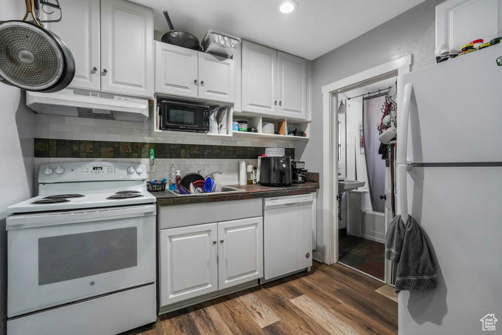 Kitchen featuring dark countertops, white appliances, under cabinet range hood, a sink, and dark wood finished floors
