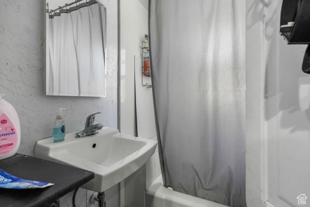 Full bath featuring a sink, a textured wall, and shower / tub combo