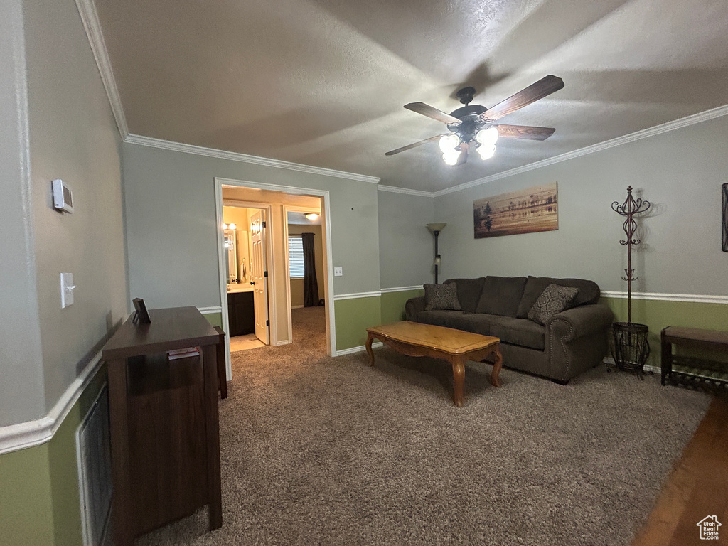 Carpeted living room featuring crown molding, a ceiling fan, and baseboards