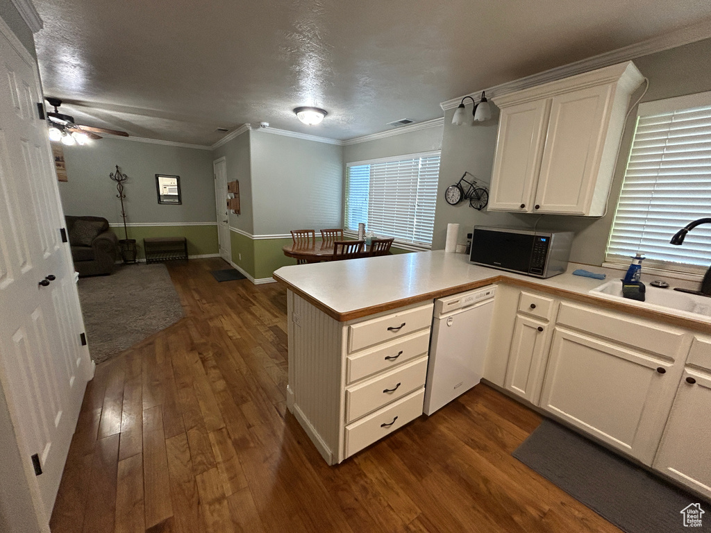 Kitchen with dark wood-style flooring, a peninsula, stainless steel microwave, a sink, and dishwasher
