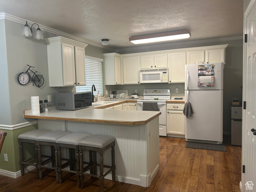 Kitchen with dark wood-style flooring, a peninsula, white appliances, white cabinetry, and a sink