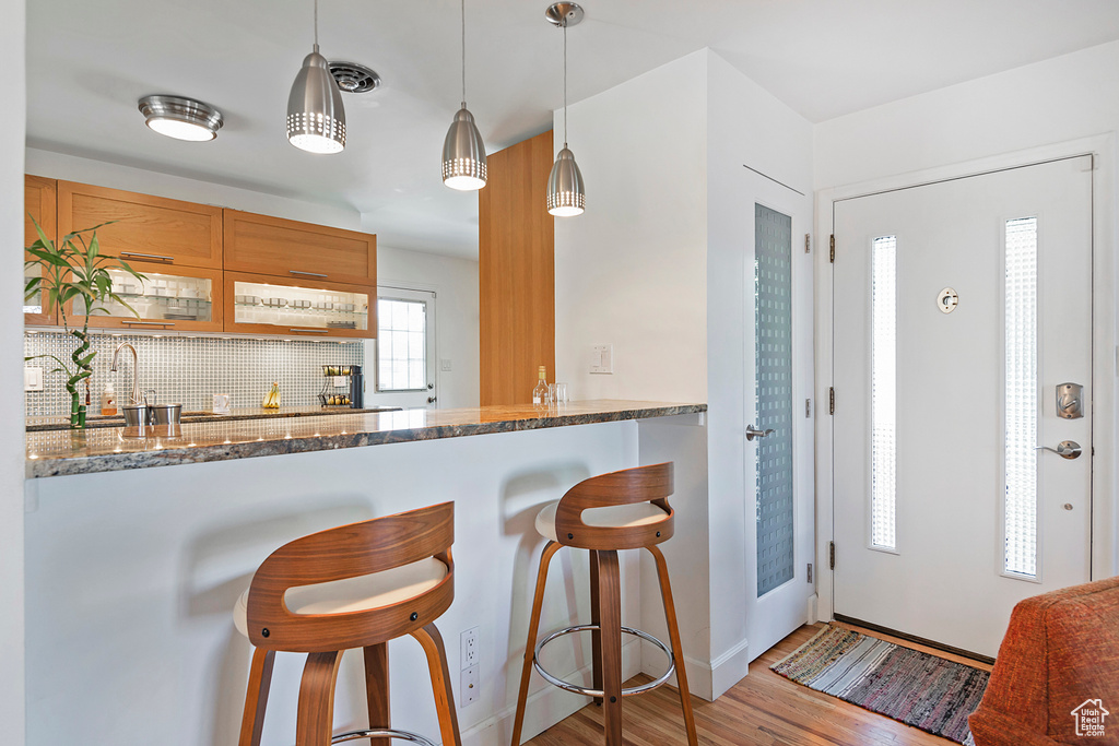 Kitchen with wood finished floors, a kitchen bar, dark stone counters, tasteful backsplash, and hanging light fixtures
