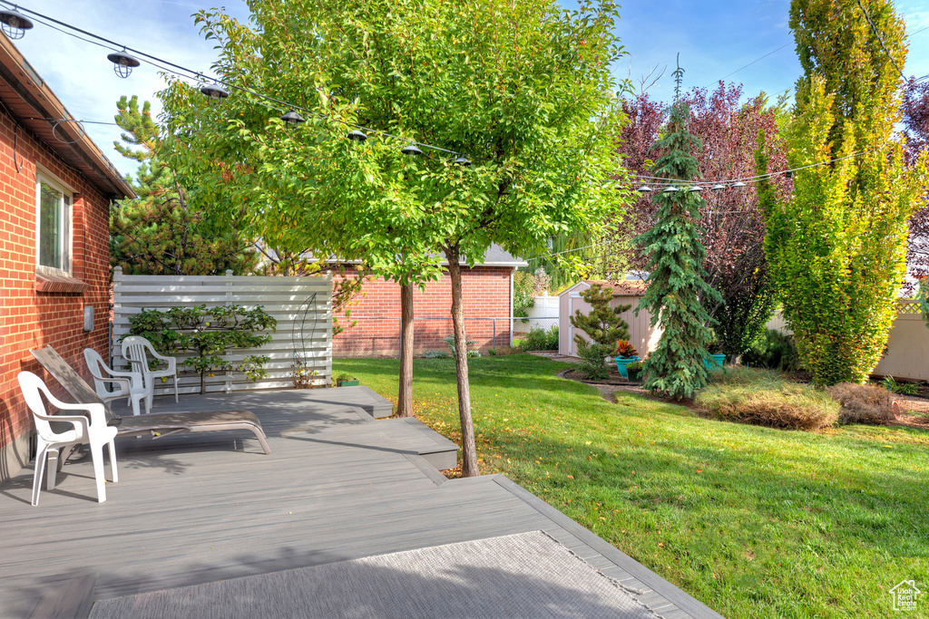 Wooden terrace with an outbuilding, a yard, fence, and a storage shed