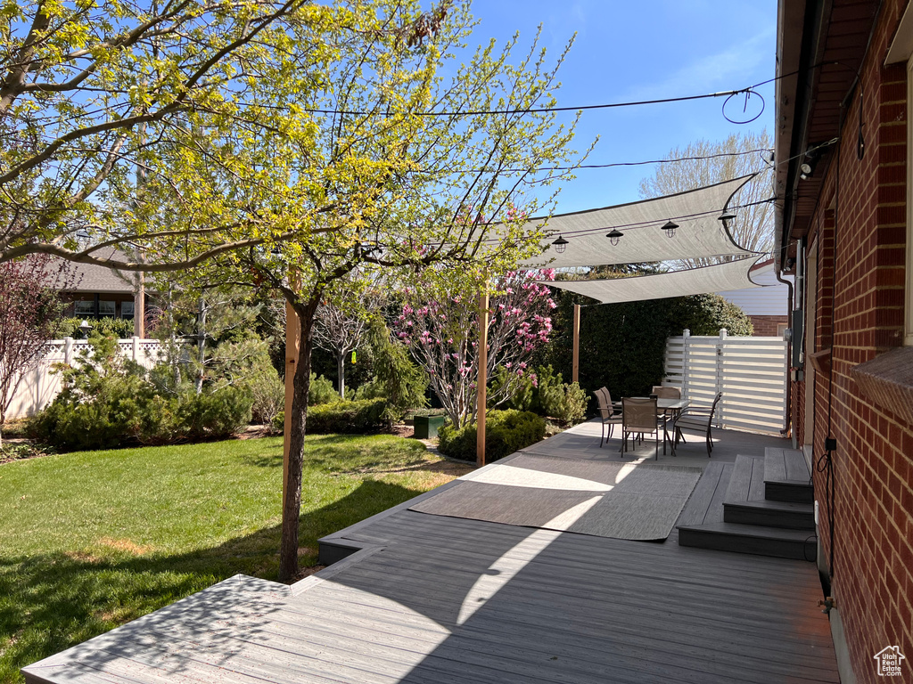 Wooden terrace with outdoor dining area, fence, and a yard