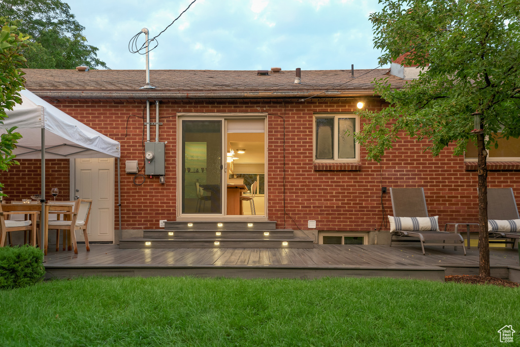 Rear view of property with a lawn, a deck, and brick siding