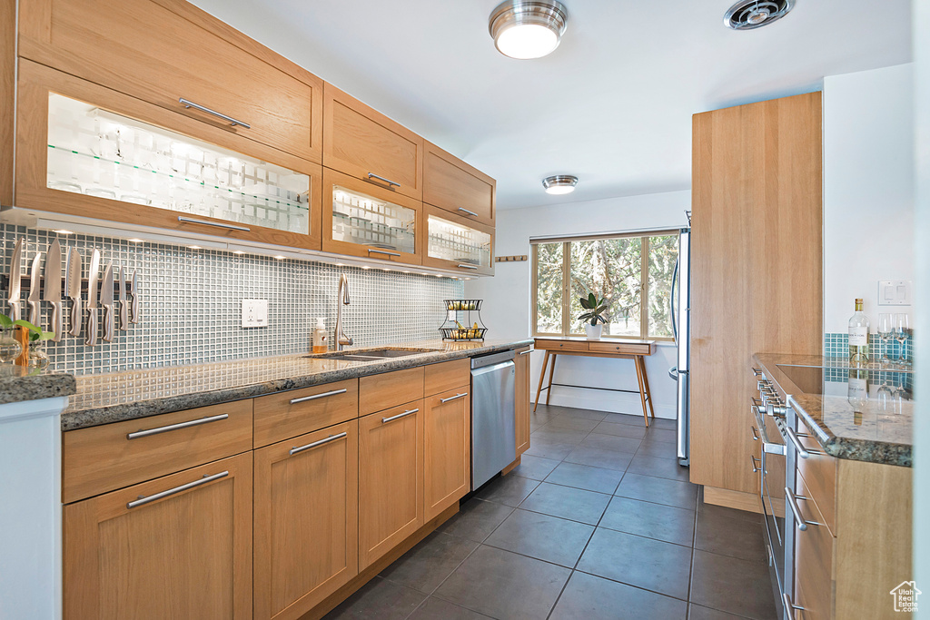 Kitchen with a sink, dishwasher, stone countertops, backsplash, and dark tile patterned floors