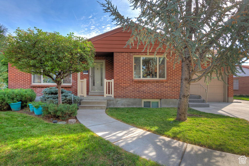 View of front of property with a garage, concrete driveway, a front lawn, and brick siding