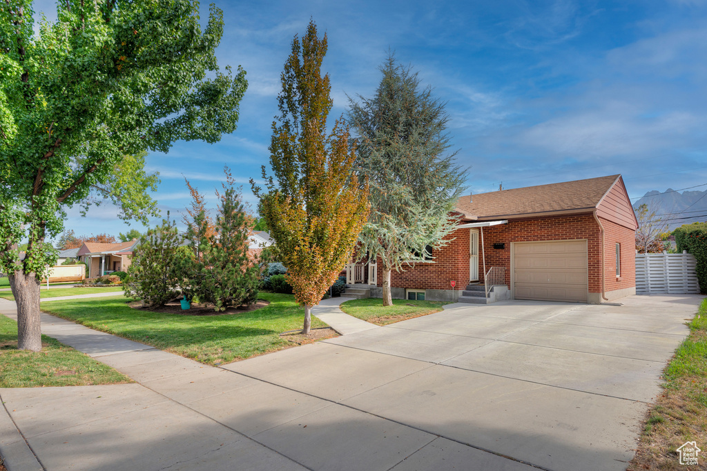 View of front of home featuring driveway, roof with shingles, brick siding, a front lawn, and an attached garage