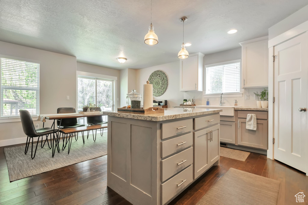 Kitchen featuring a sink, gray cabinets, dark wood-type flooring, a kitchen island, and pendant lighting