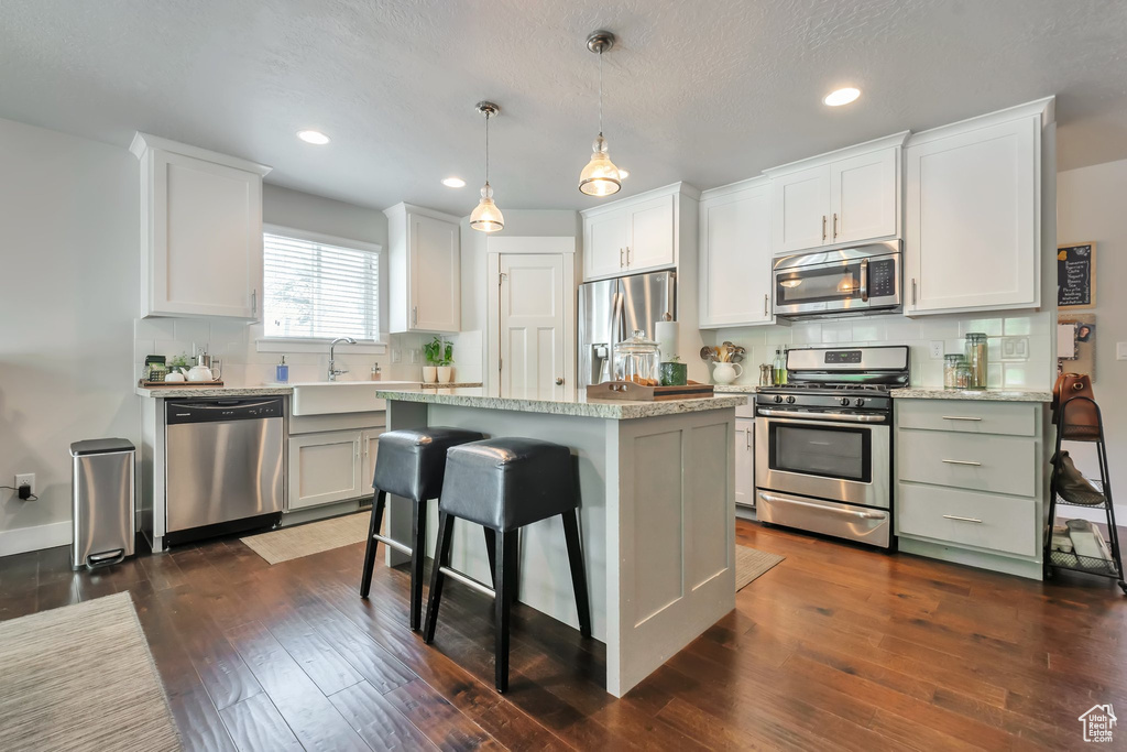 Kitchen with dark wood-style flooring, appliances with stainless steel finishes, a center island, recessed lighting, and tasteful backsplash