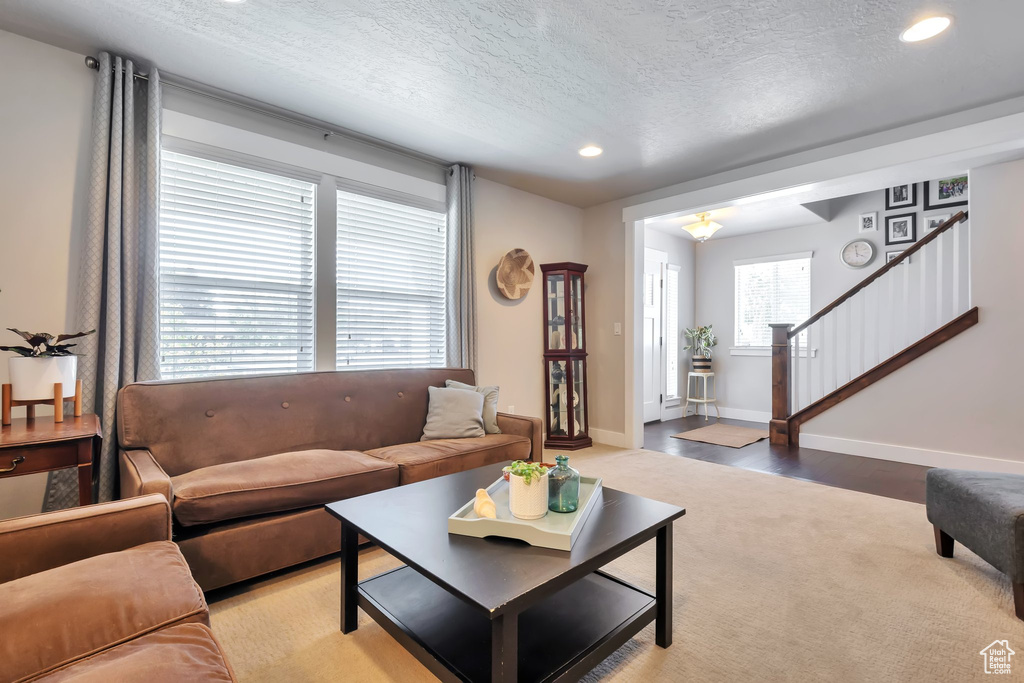 Living room with light colored carpet, a textured ceiling, stairs, recessed lighting, and baseboards