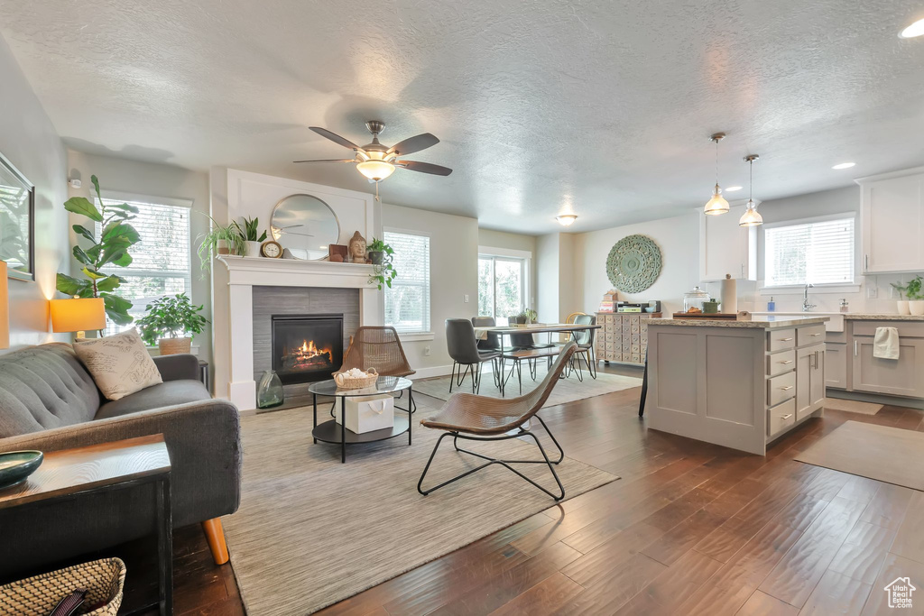 Living area with a ceiling fan, a textured ceiling, a glass covered fireplace, and dark wood-type flooring