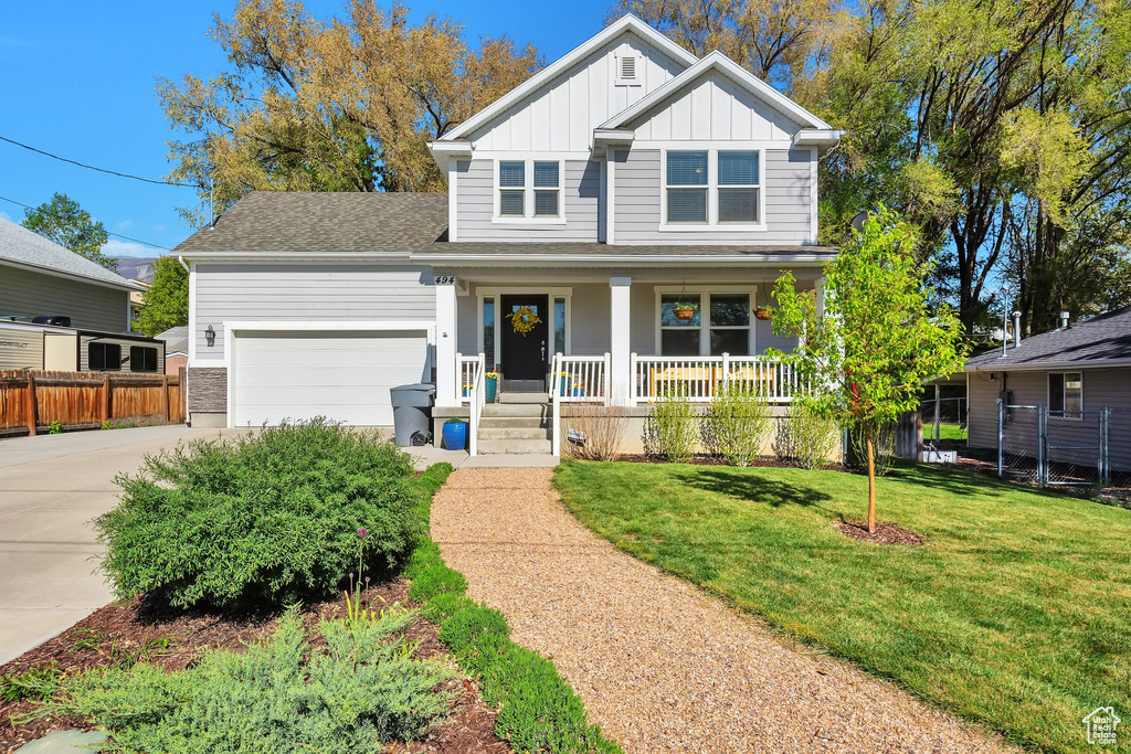 View of front facade featuring board and batten siding, a porch, driveway, a front yard, and an attached garage