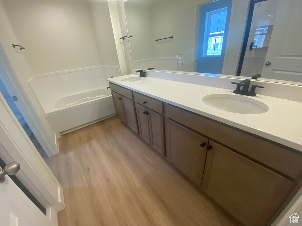Bathroom with double vanity, a sink, a bath, and wood finished floors