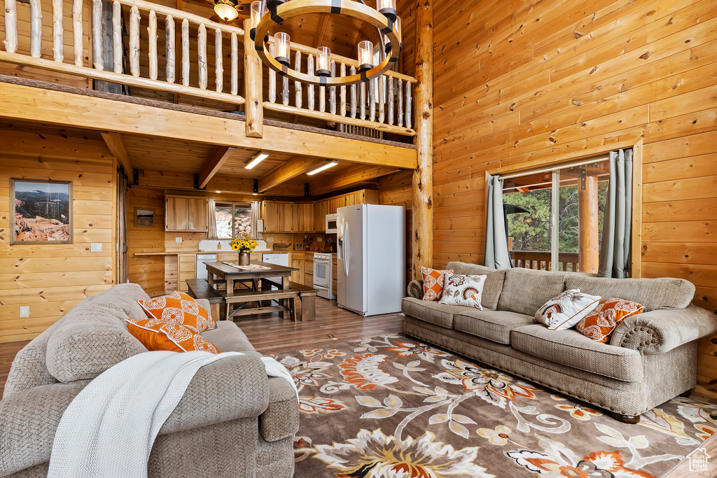 Living room featuring wooden walls, a notable chandelier, beam ceiling, light wood finished floors, and wood ceiling