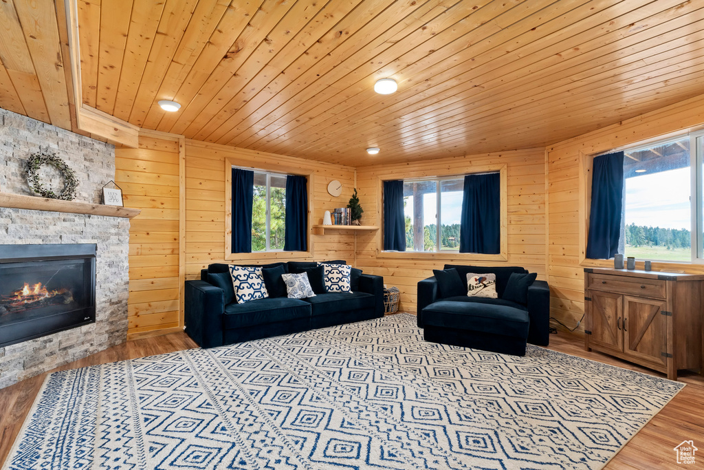 Living room with a stone fireplace, wood ceiling, wood finished floors, and wooden walls