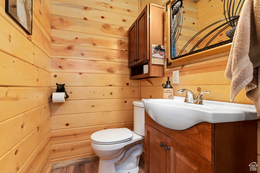 Bathroom featuring toilet, wood walls, wood finished floors, and vanity