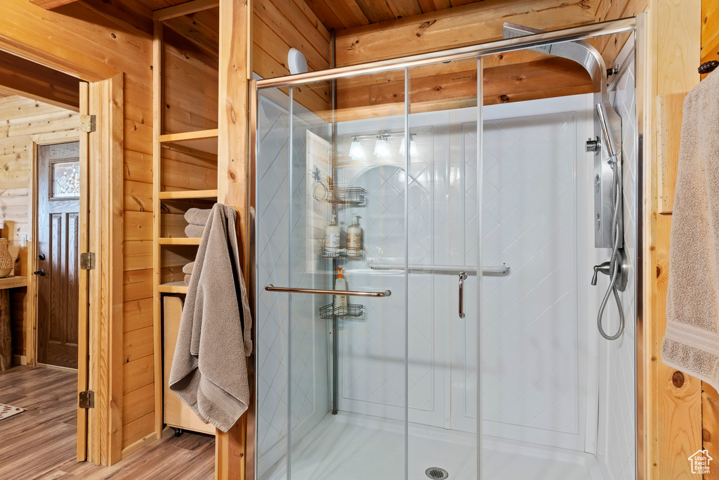 Bathroom with wood walls, a shower stall, and wood finished floors