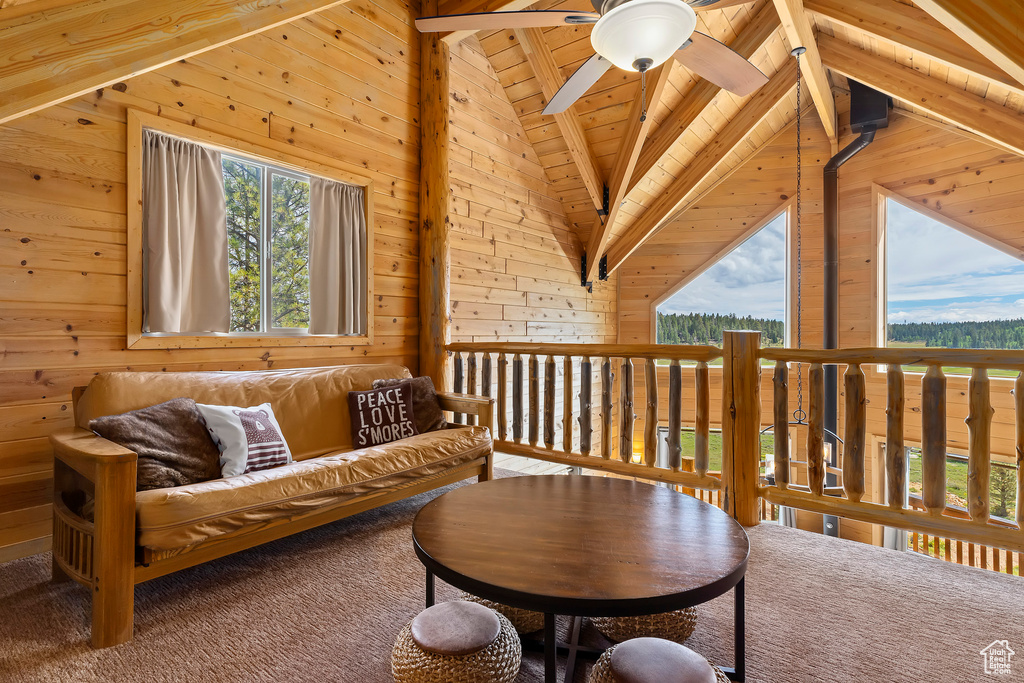 Sitting room with wood walls, lofted ceiling with beams, ceiling fan, and carpet