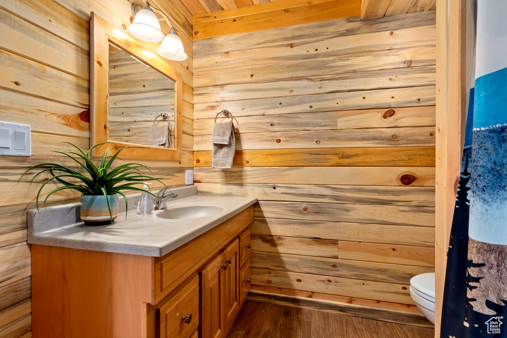 Half bathroom featuring vanity, toilet, wood walls, and wood finished floors