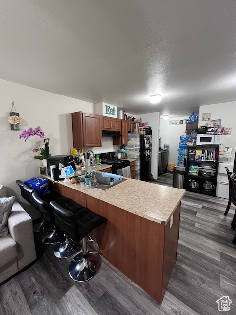 Kitchen featuring light countertops, gas range, freestanding refrigerator, a peninsula, and dark wood-type flooring