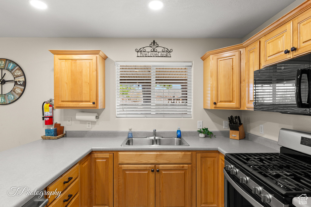 Kitchen featuring stainless steel range with gas cooktop, a sink, black microwave, and light countertops
