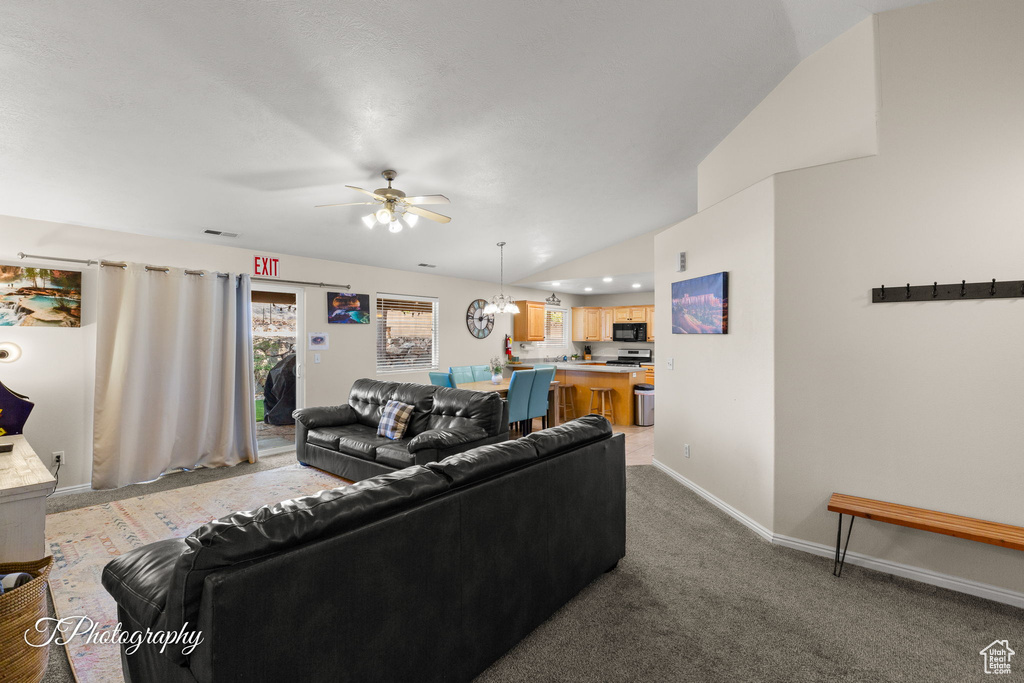Carpeted living room with baseboards, ceiling fan with notable chandelier, vaulted ceiling, and visible vents