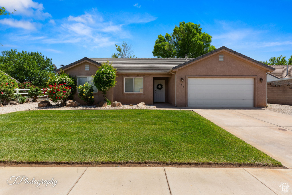 Single story home with a garage, a front yard, stucco siding, a tiled roof, and concrete driveway