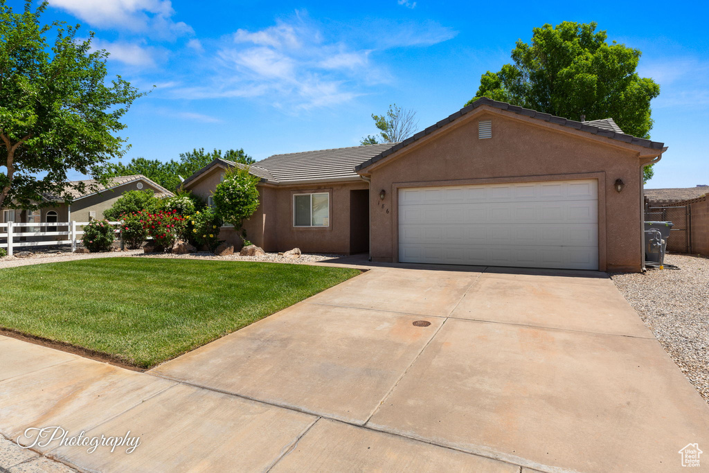 Ranch-style house featuring fence, a tiled roof, an attached garage, and a front lawn