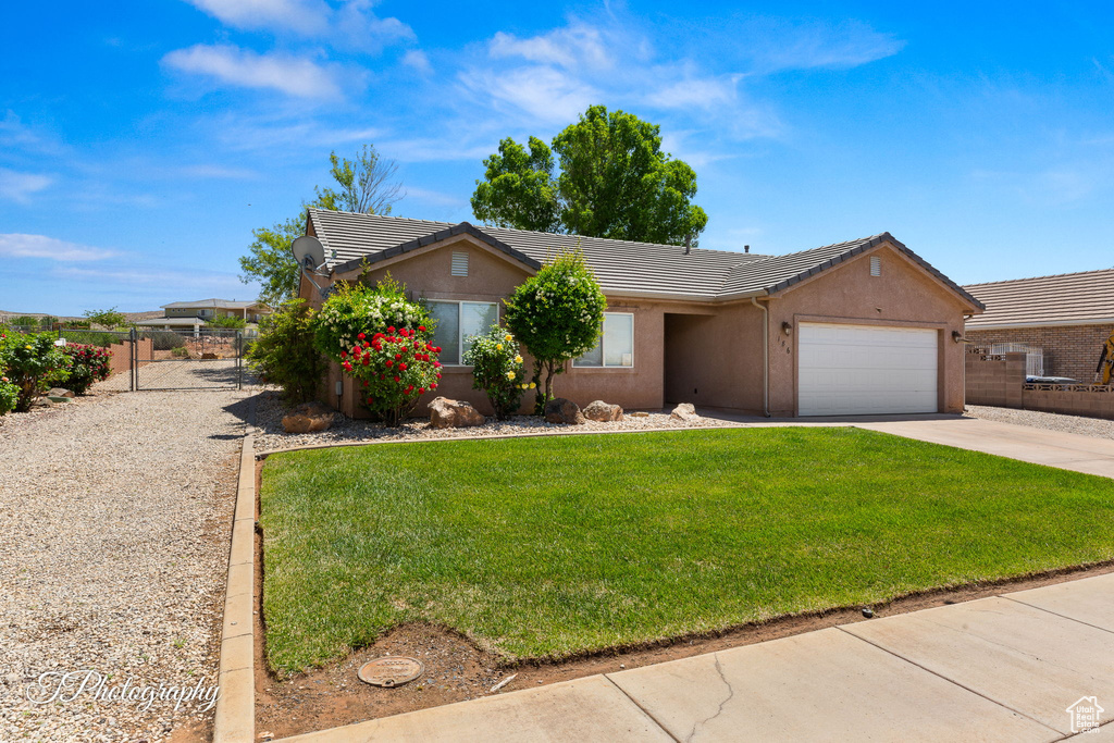 Single story home with a tile roof, a garage, a front lawn, concrete driveway, and stucco siding