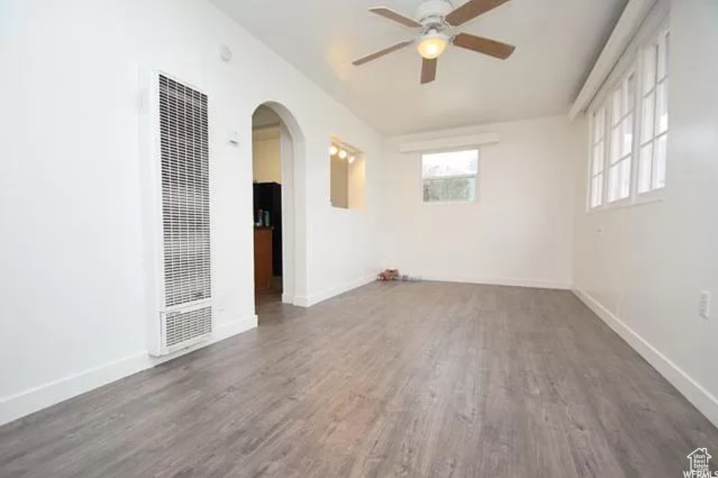 Spare room featuring a heating unit, wood finished floors, baseboards, ceiling fan, and arched walkways