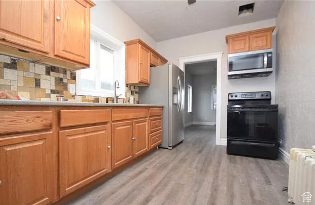 Kitchen featuring appliances with stainless steel finishes, tasteful backsplash, baseboards, radiator, and light wood-style flooring