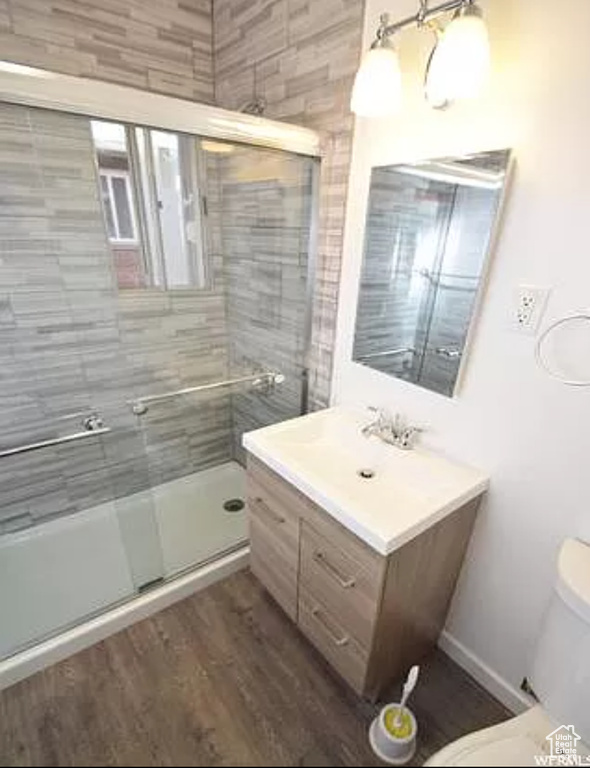 Bathroom featuring vanity, toilet, wood finished floors, and a stall shower