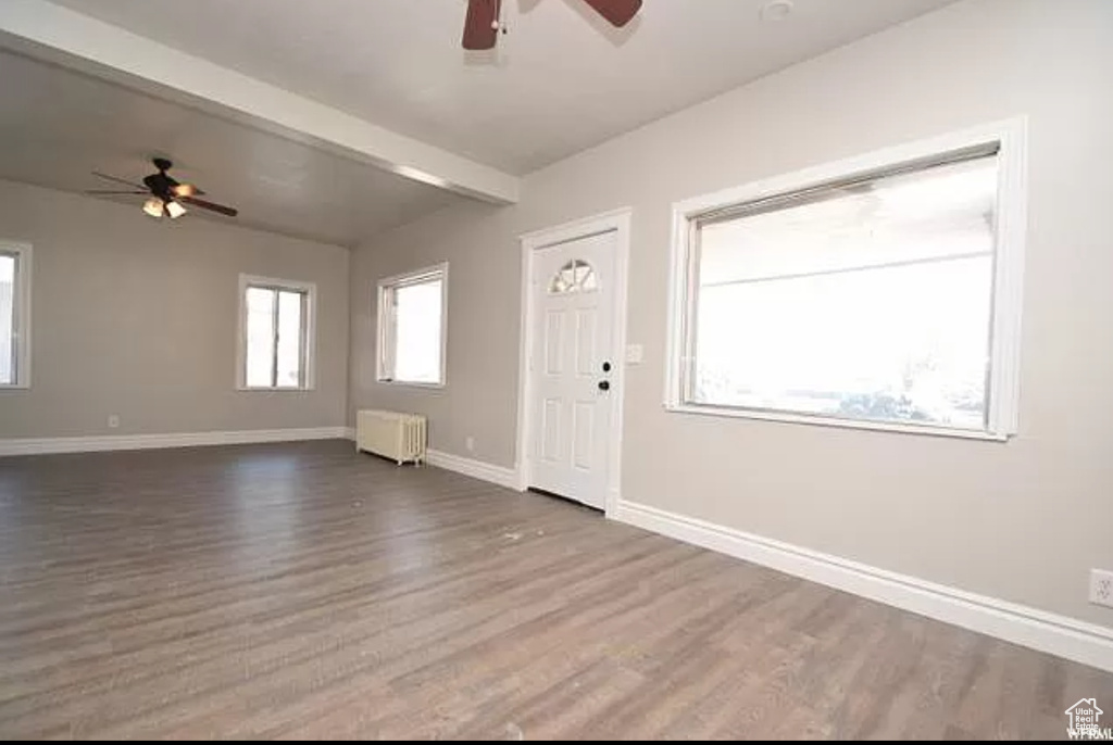 Interior space with a ceiling fan, beam ceiling, baseboards, dark wood-style floors, and radiator