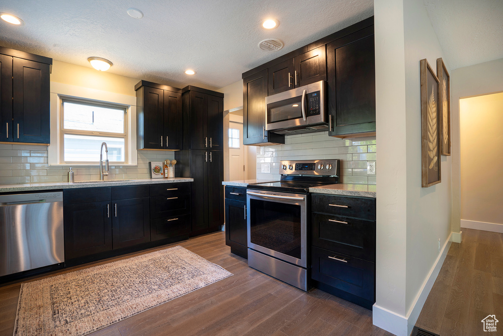 Kitchen with a sink, baseboards, stainless steel appliances, and dark wood-type flooring