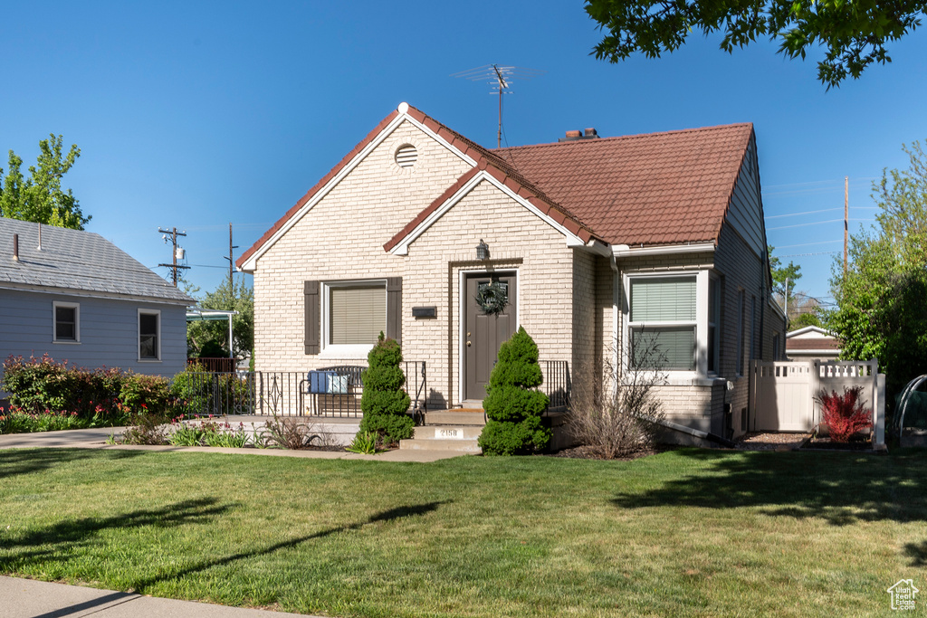 Bungalow-style home featuring a tile roof, a front lawn, and brick siding