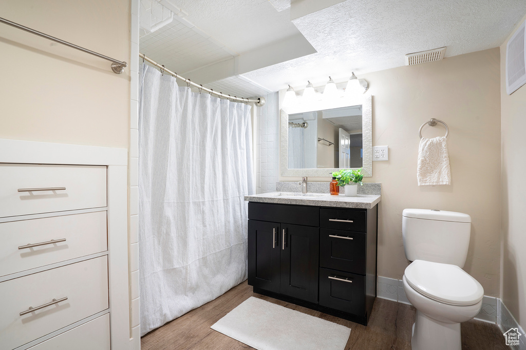 Bathroom featuring a shower with curtain, visible vents, wood finished floors, vanity, and toilet