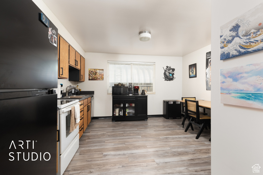 Kitchen featuring dark countertops, a sink, light wood-style floors, brown cabinetry, and black appliances
