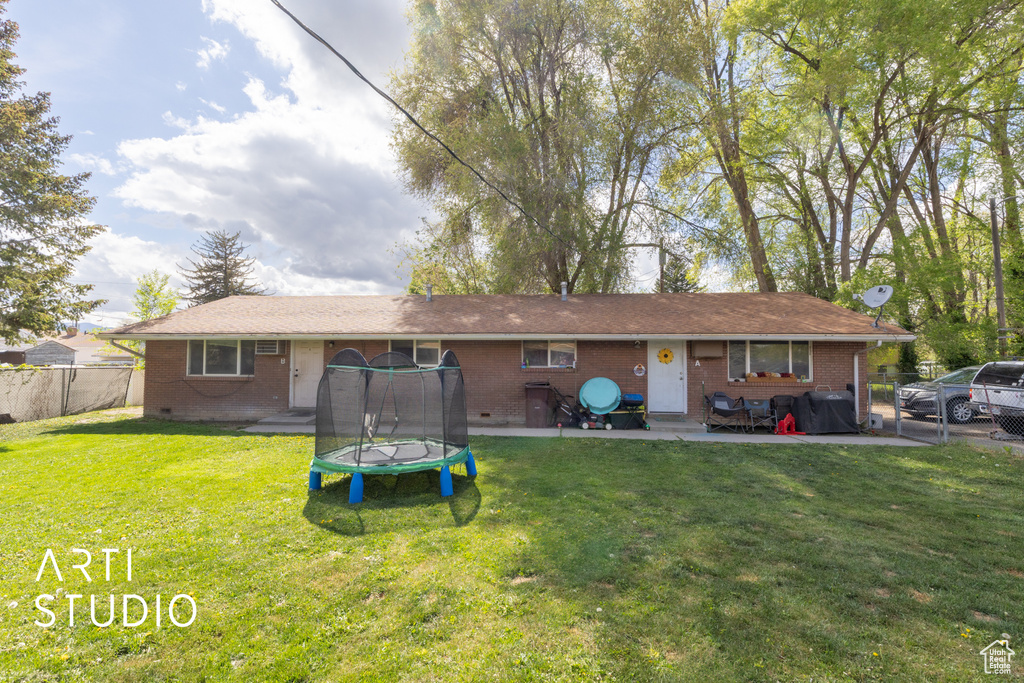Back of house featuring brick siding, a trampoline, fence, and a yard