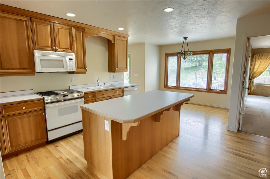 Kitchen with a kitchen island, white appliances, light countertops, a sink, and light wood finished floors
