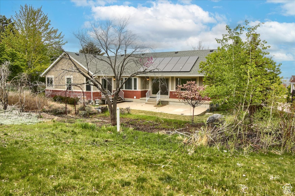 Rear view of house with brick siding, roof mounted solar panels, and roof with shingles
