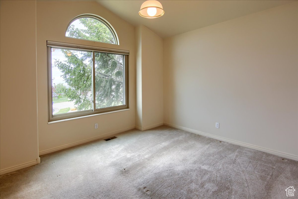 Carpeted spare room featuring baseboards, lofted ceiling, and visible vents