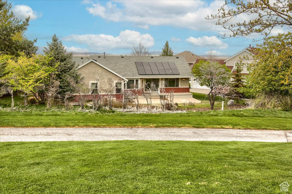Rear view of property with a lawn, stucco siding, solar panels, and roof with shingles