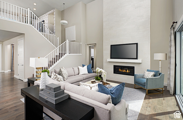 Living area with stairs, wood finished floors, a towering ceiling, a fireplace, and baseboards