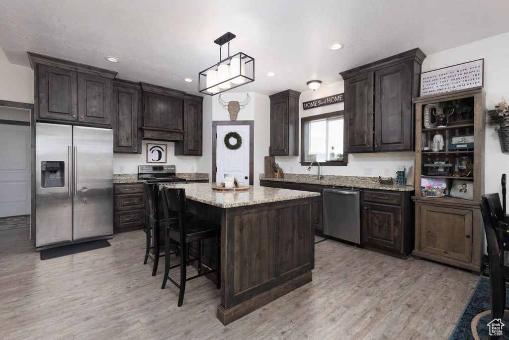 Kitchen with appliances with stainless steel finishes, dark brown cabinetry, light wood finished floors, and a center island
